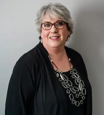 A woman with short hair and glasses wearing a black shirt.