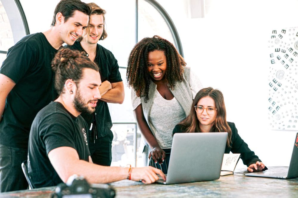 A group of people standing around a laptop.